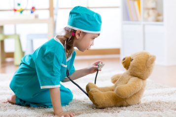 Dziewczynka bawiąca się z misiem, udająca, że jest lekarzem w szpitalu