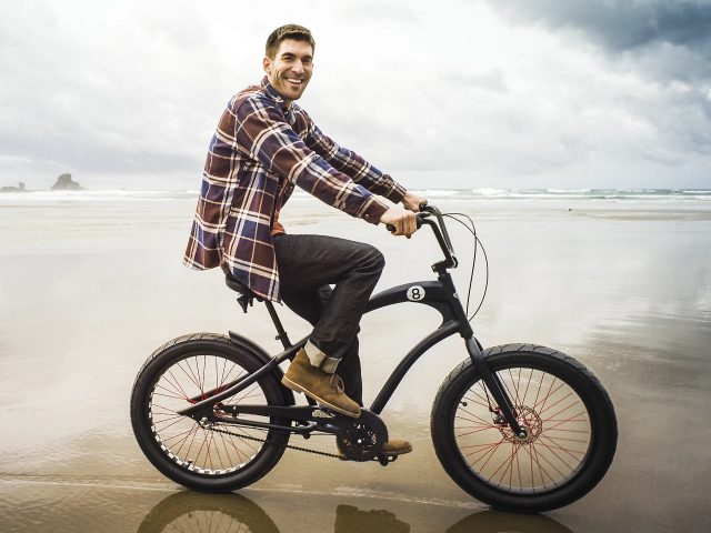 Mężczyzna na czarnym rowerze elektrycznym Electra na plaży